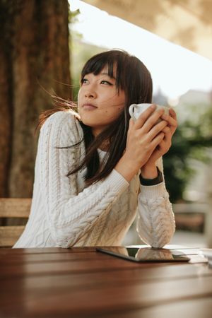 Young woman sitting at table wearing cream sweater holding mug