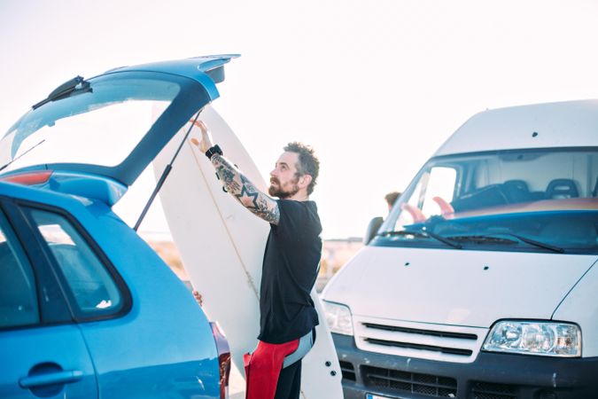 Man loading surfboard into back of vehicle
