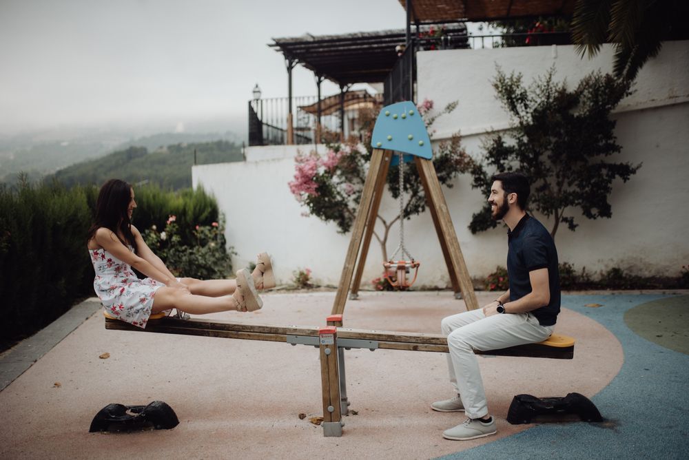 Playful couple swinging on seesaw on playground at rural street