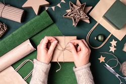 Woman’s hands tying twine on winter gift box with festive wrapping items around