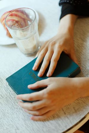 Person holding blue book near clear drinking glass on table