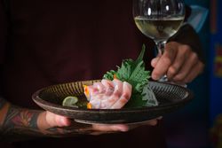 Crop chef serving sea bass sashimi with wineglass