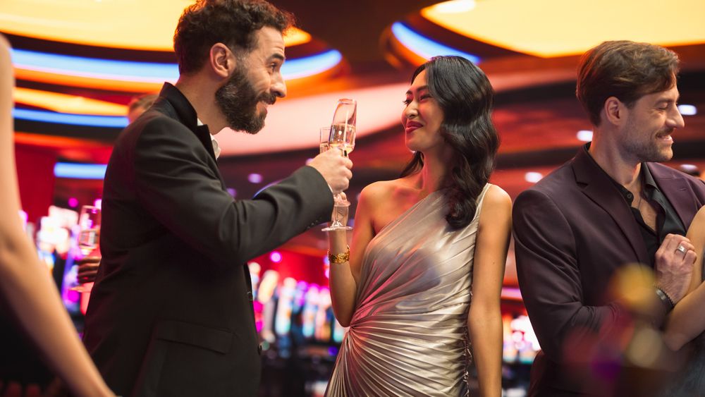 Multiethnic Couple Having a Fun Conversation at a Casino while Drinking Champagne and Gambling at a Roulette Table.