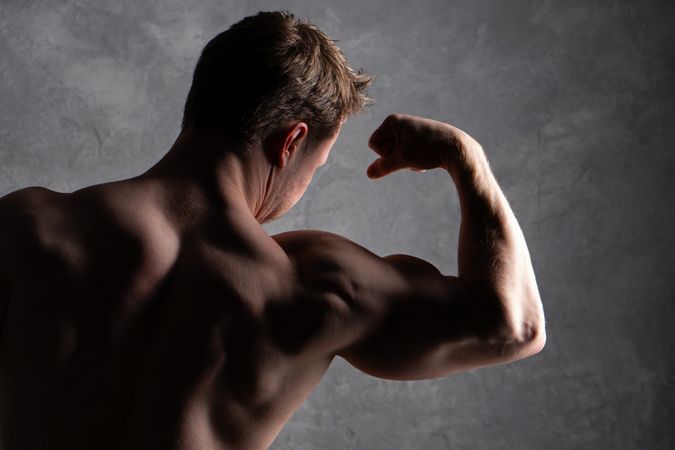 Shirtless man flexing bicep, strong lighting on muscular back.