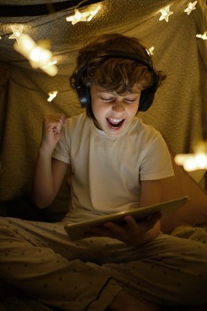 Cheerful boy watching match on tablet in blanket fort