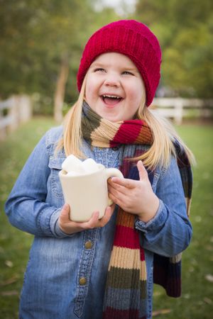 Cute Young Girl Holding Cocoa Mug with Marsh Mallows Outside