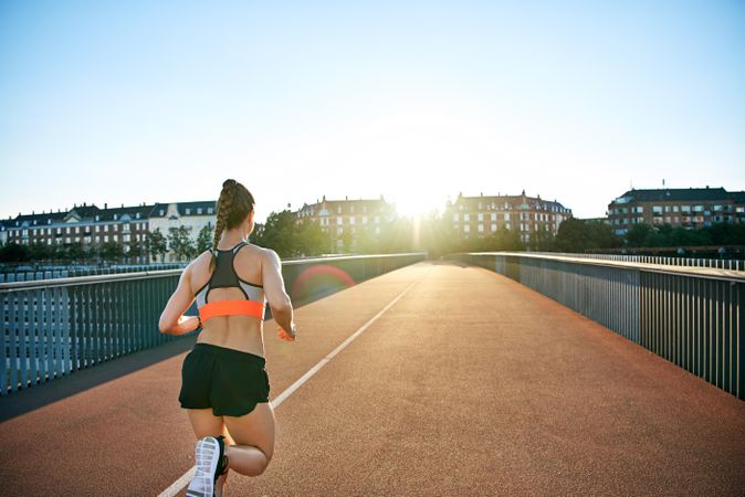 Back show of athletic woman running across a European bridge