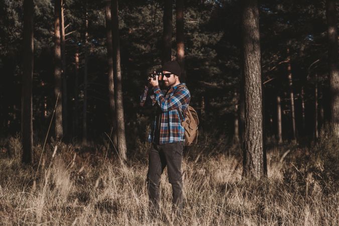 Confident photographer taking picture with camera in sunny forest