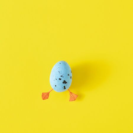 Blue egg with duck legs on yellow background