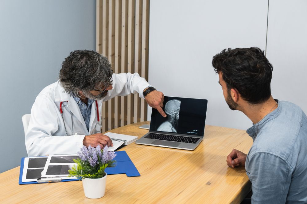 Mature doctor and patient discussing x ray on laptop in medical office