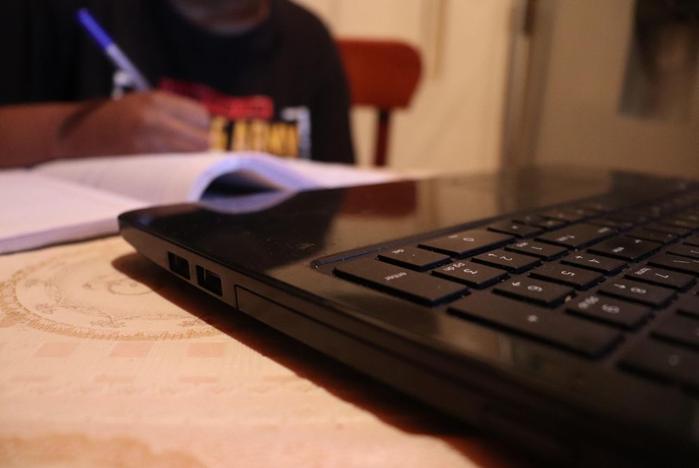 Cropped image of a person writing on a notebook near computer