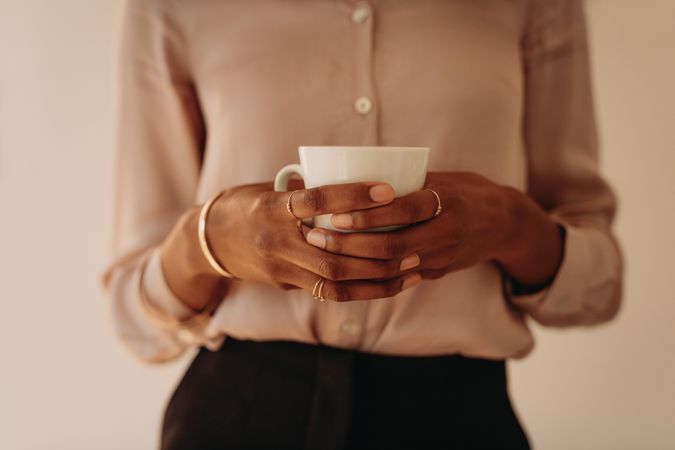 Close up of the hands of a Black woman in blouse holding a mug