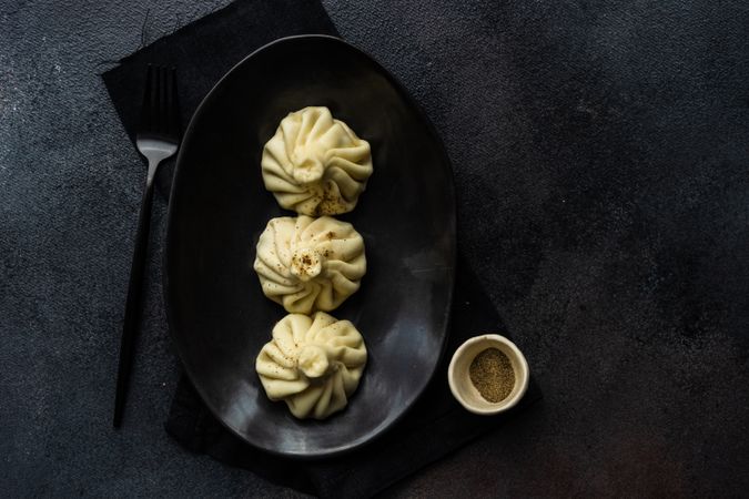 Top view of plate of three Georgian khinkali dumplings on dark plate and table