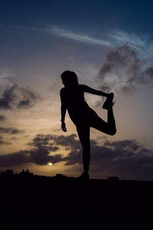 Stretching woman and sky with clouds at sunset