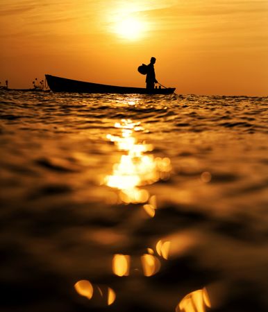 Man riding a boat in water during golden hour