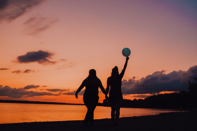 Unrecognizable females walking along beach during sunset