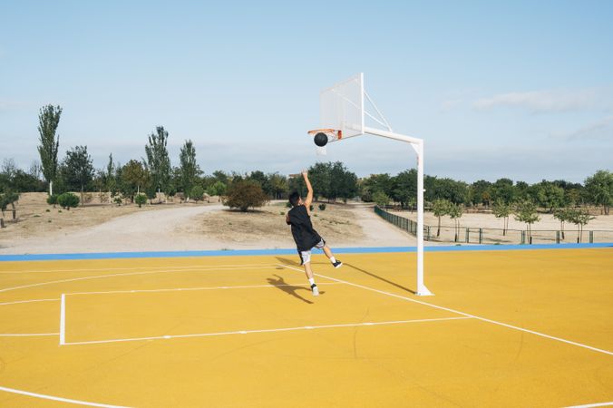 Young man playing on yellow basketball court outdoor.