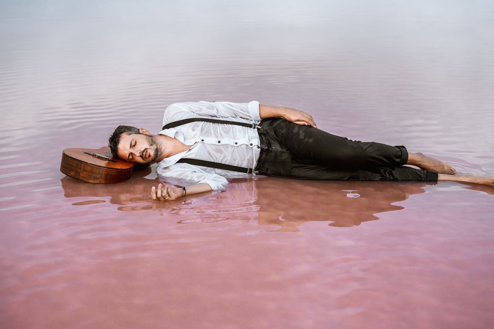 Man resting in water with guitar at seaside