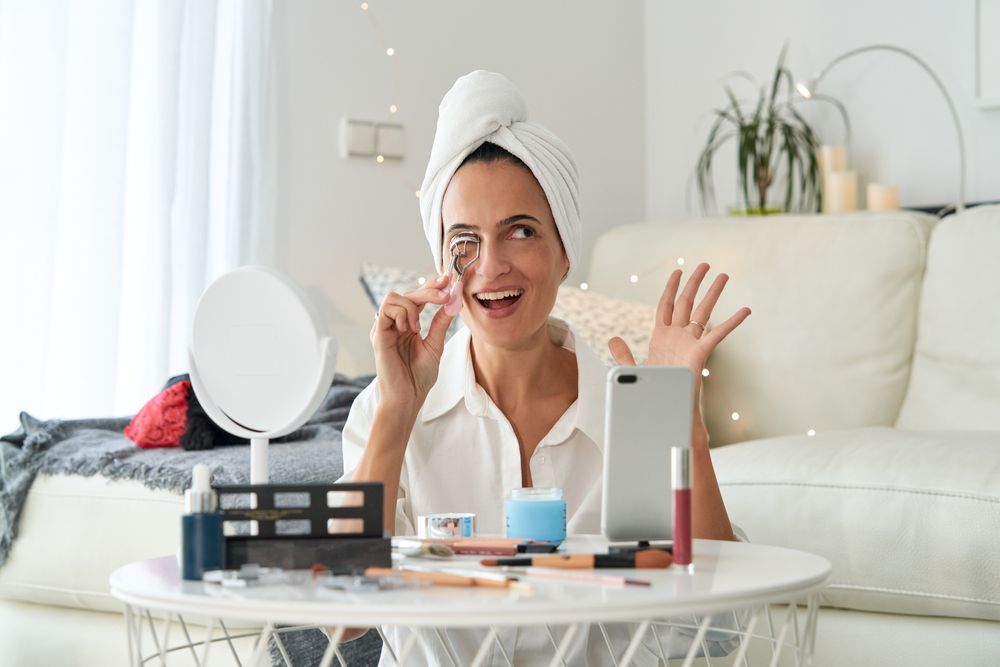 Delighted female with eyelash curler and phone