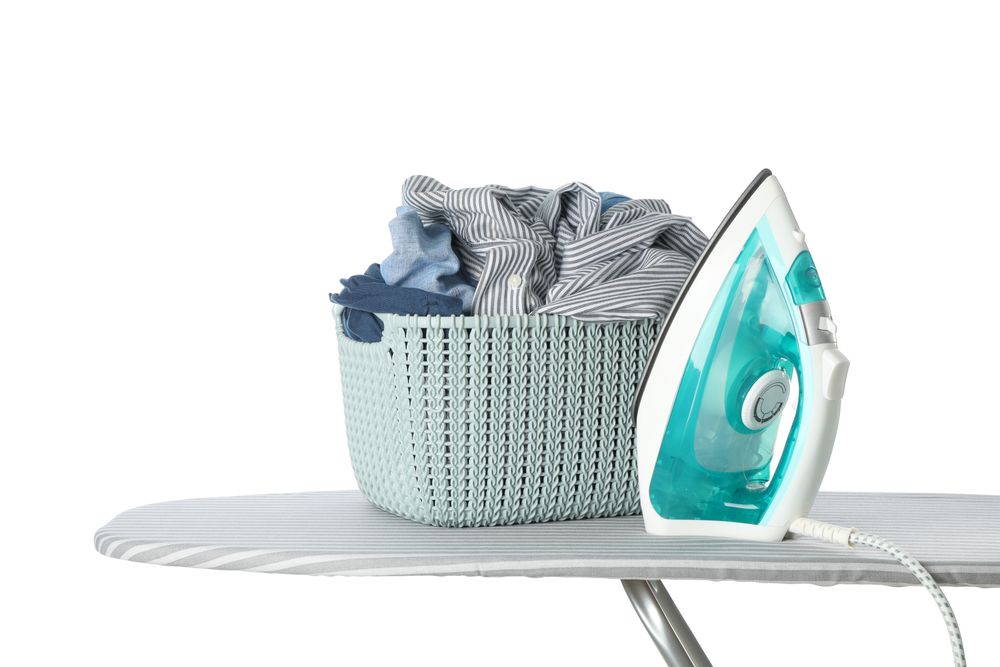 Iron and basket with clothes on ironing board isolated on blank background