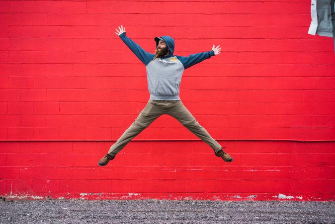 Bearded guy jumping near red wall