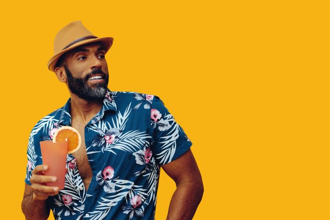 Happy male holding a cocktail while wearing colorful shirt with yellow background, copy space
