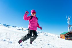 Child in pink snow suit jumping for joy on snowy hill