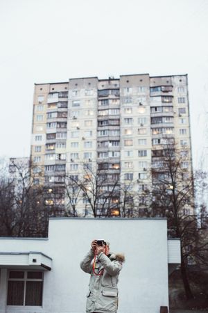 Man taking photo in front of apartment blocks on an overcast day