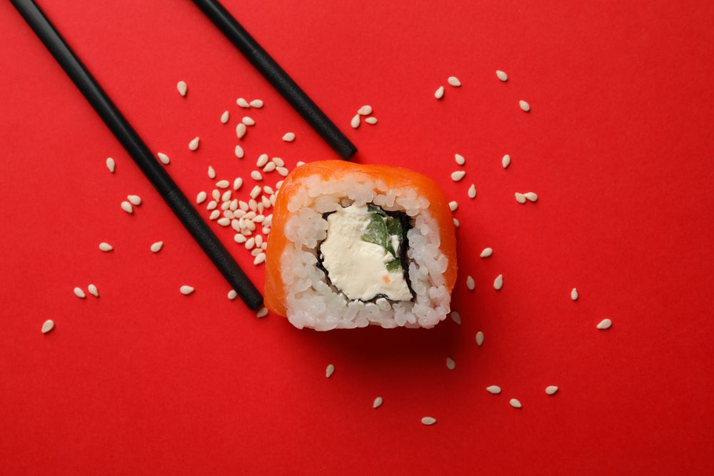 Chopsticks and sushi roll on red background, top view