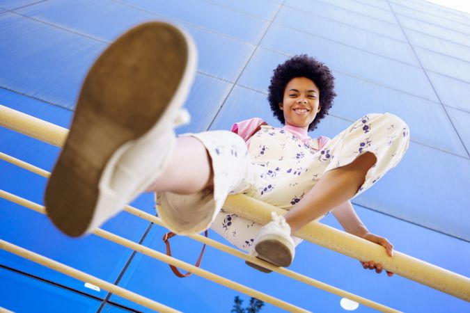 Low angle shot of happy woman sitting on handrails in front of  reflective glass building