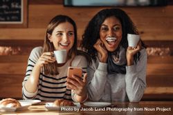 Two women drinking coffee and smiling with a milk mustache in coffee shop 5l3gN0