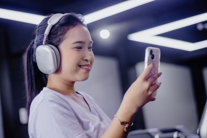 Smiling Asian Woman Enjoys Music with Headphones and Mobile Phon