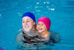 Cheerful girl swimming in pool with mother