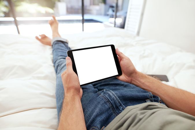 Closeup image of man lying on a bed holding a digital tablet