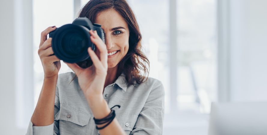 Happy woman taking pictures with her dslr camera indoors