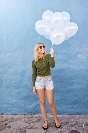 Young woman holding white balloons against blue wall