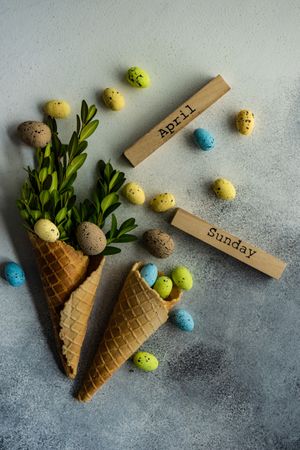 Top view of Easter card concept with green branch in waffle cone with decorative eggs