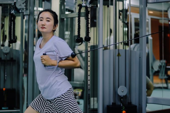 A woman is actively exercising on a cable machine inside a fitness center