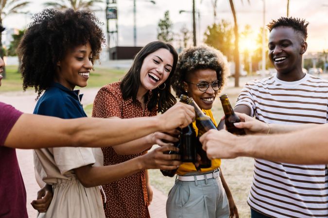 Happy multi-ethnic friends toasting with beer bottles at sunset