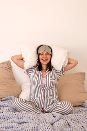 Woman laughing in bed, hands behind head with eye mask.