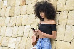 Female texting while leaning on outside wall, copy space