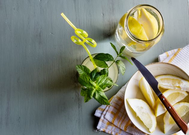 Glass of fresh lemonade next to plate with cut lemons on table