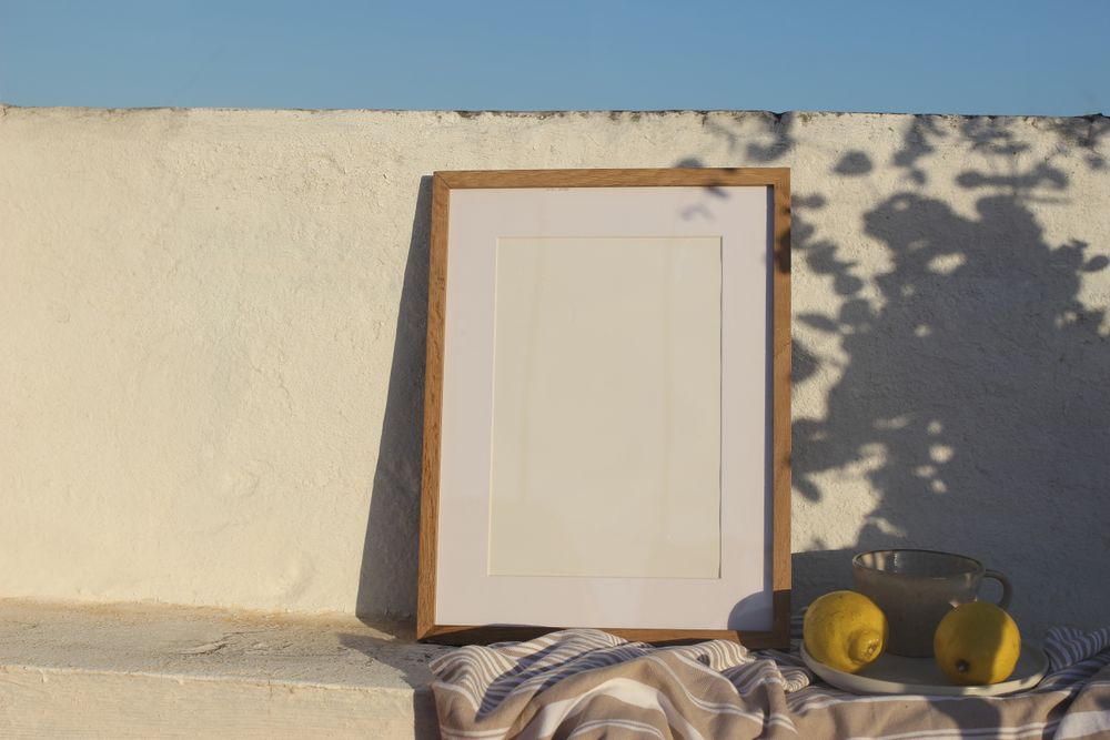 Vertical wooden frame picture mockup against white old textured wall in sunlight.