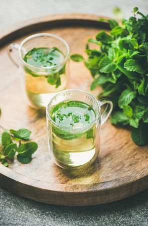 Mint tea with fresh mint leaves on wooden tray, selective focus
