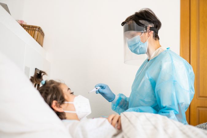 Girl in facemask in hospital bed with doctor caring for her