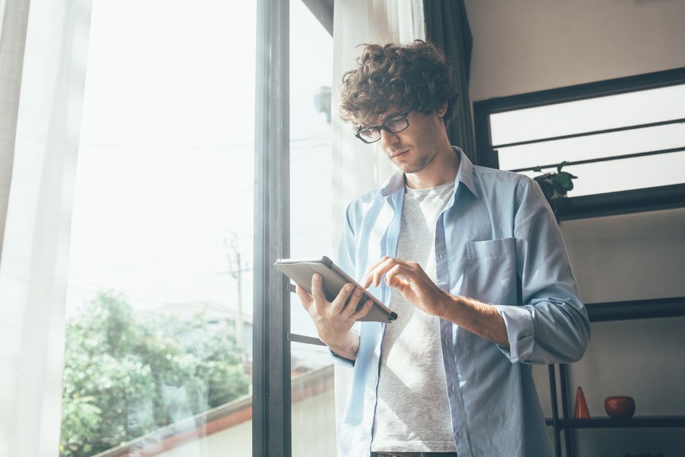 Creative designer using digital tablet working at home standing by window