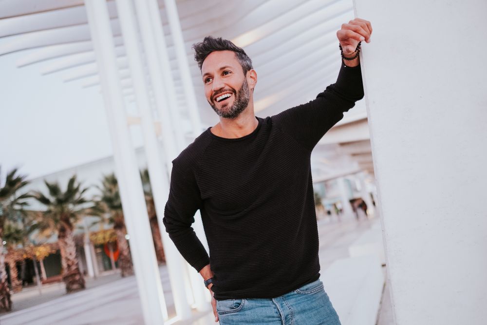 Adult stylish smiling man near grey wall on street