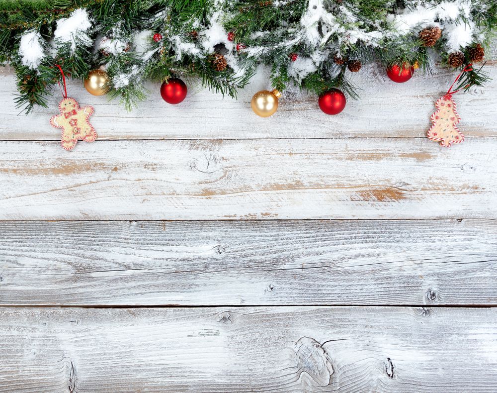 Top border of snowy Christmas evergreen branches with other holiday decorations on rustic wooden boards