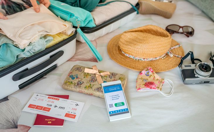 Woman preparing suitcase for vacation and mobile phone with covid green pass
