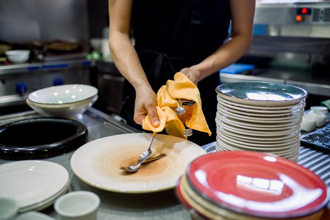 Crop woman cleaning cutleries and plates in kitchen